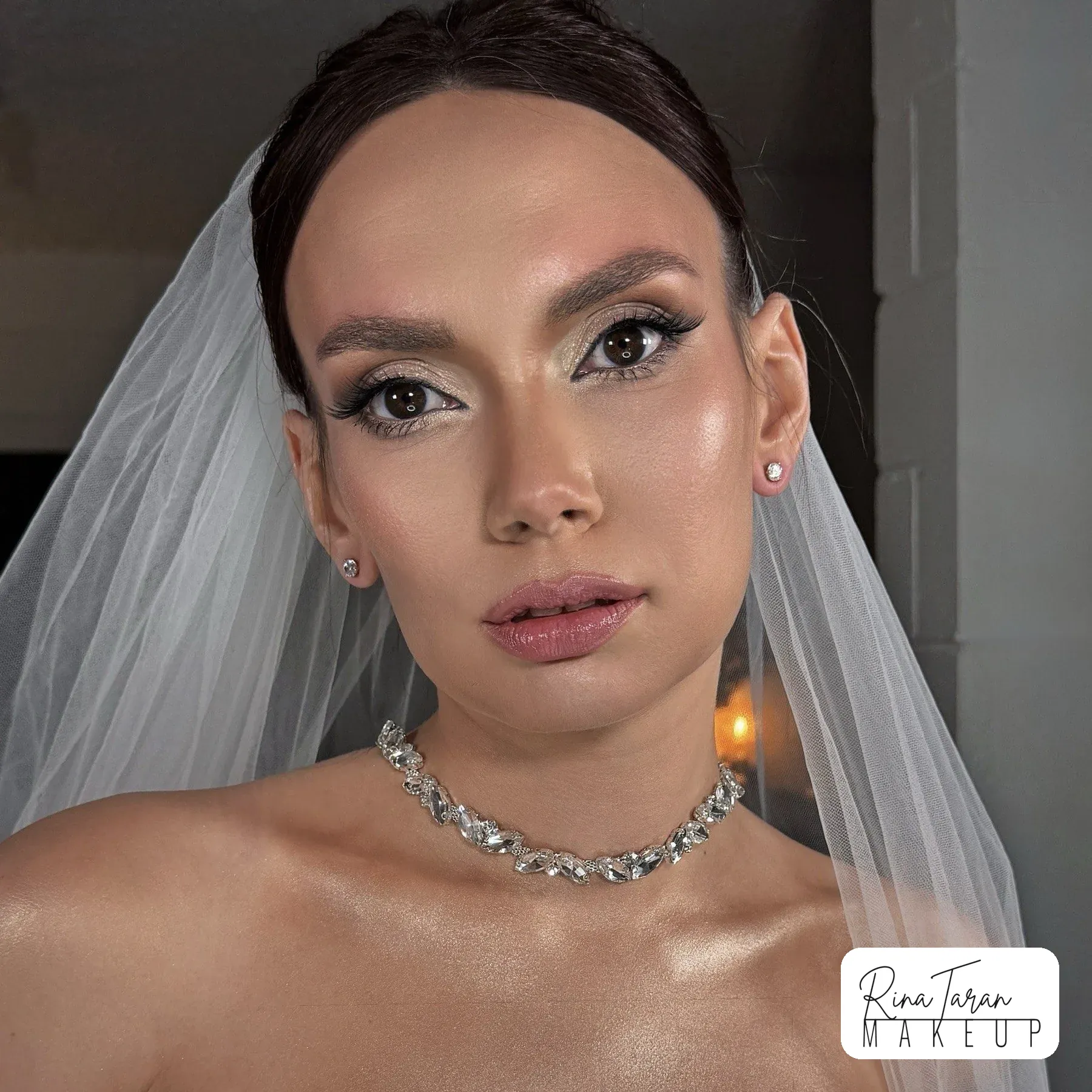 Bridal makeup with a shimmer lid, winged liner and a glossy nude lip under a veil