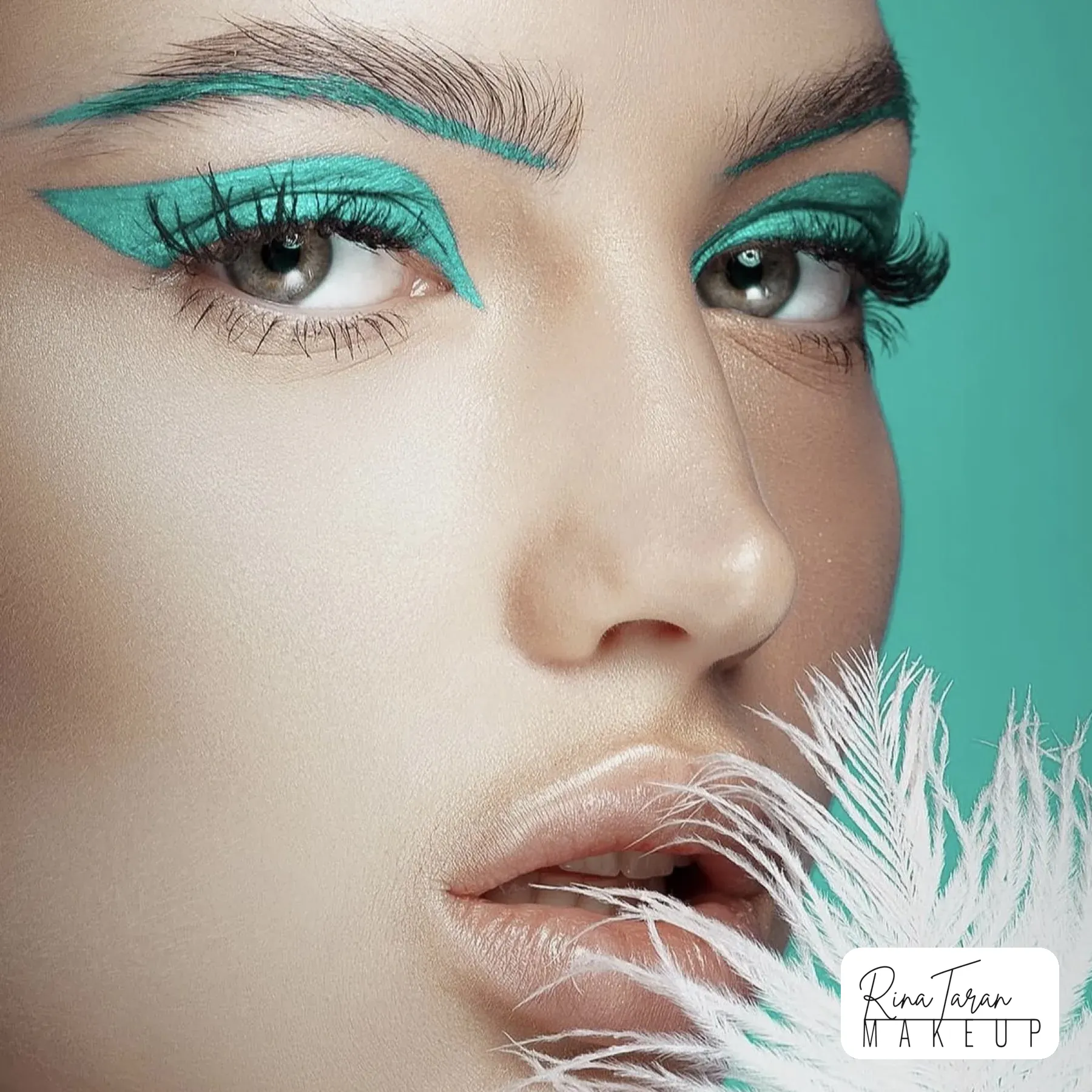 Turquoise graphic liner carried up onto the brow, beauty editorial with a feather