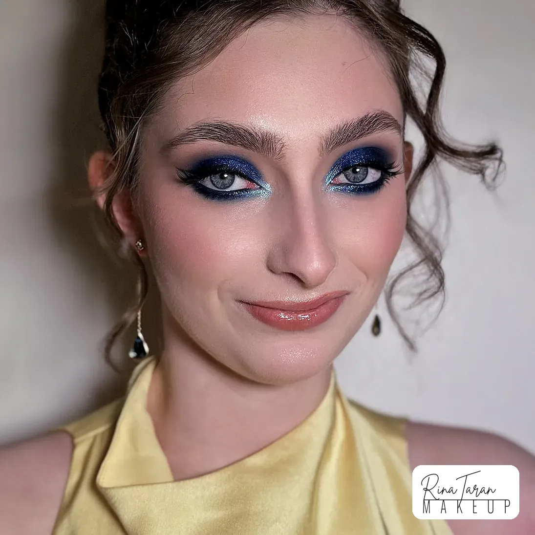 A bold formal look built around a blue eye, finished with a glossy nude lip