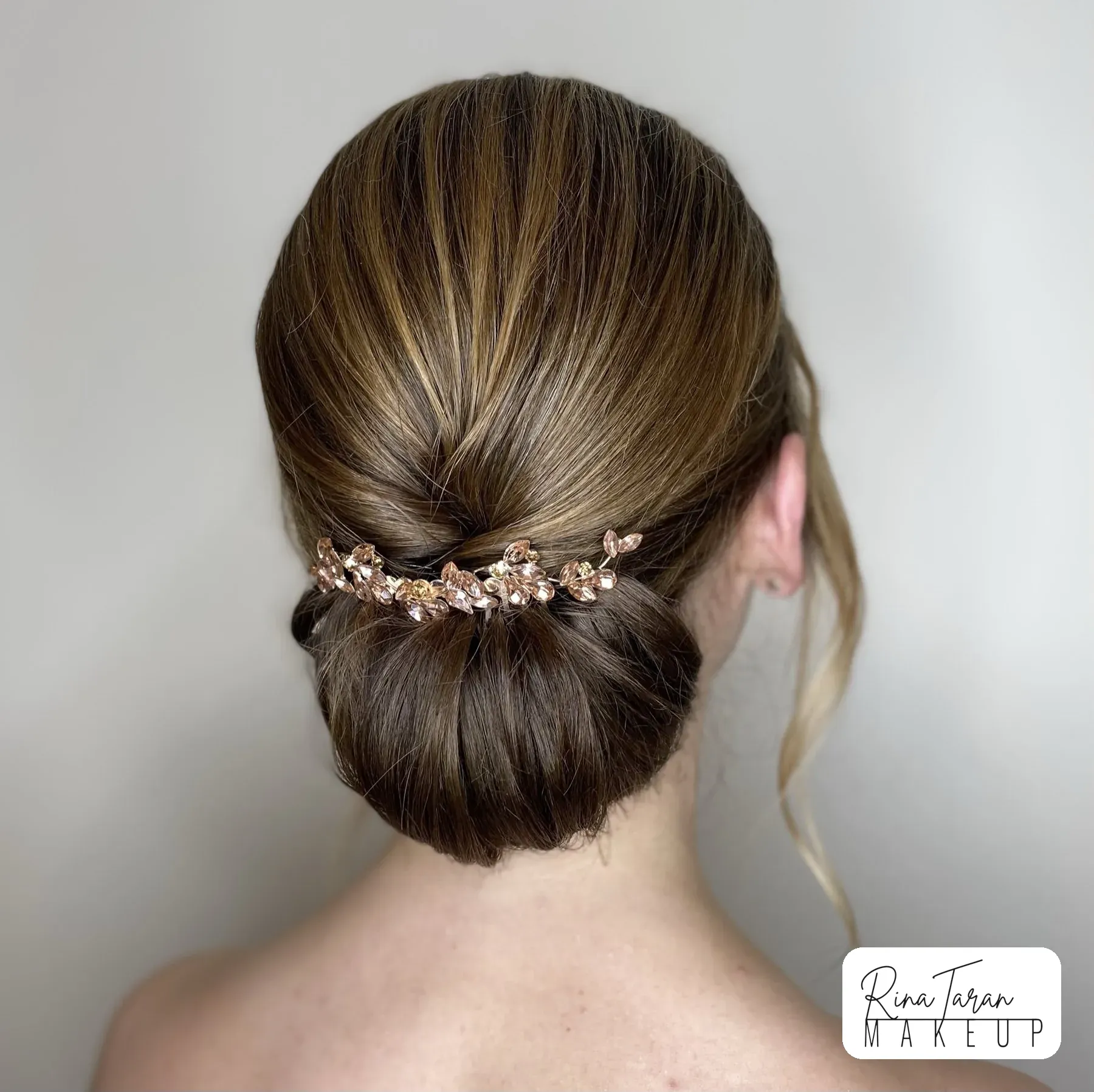 Sleek low chignon with a gold floral hairpiece, bridal and event hair styling