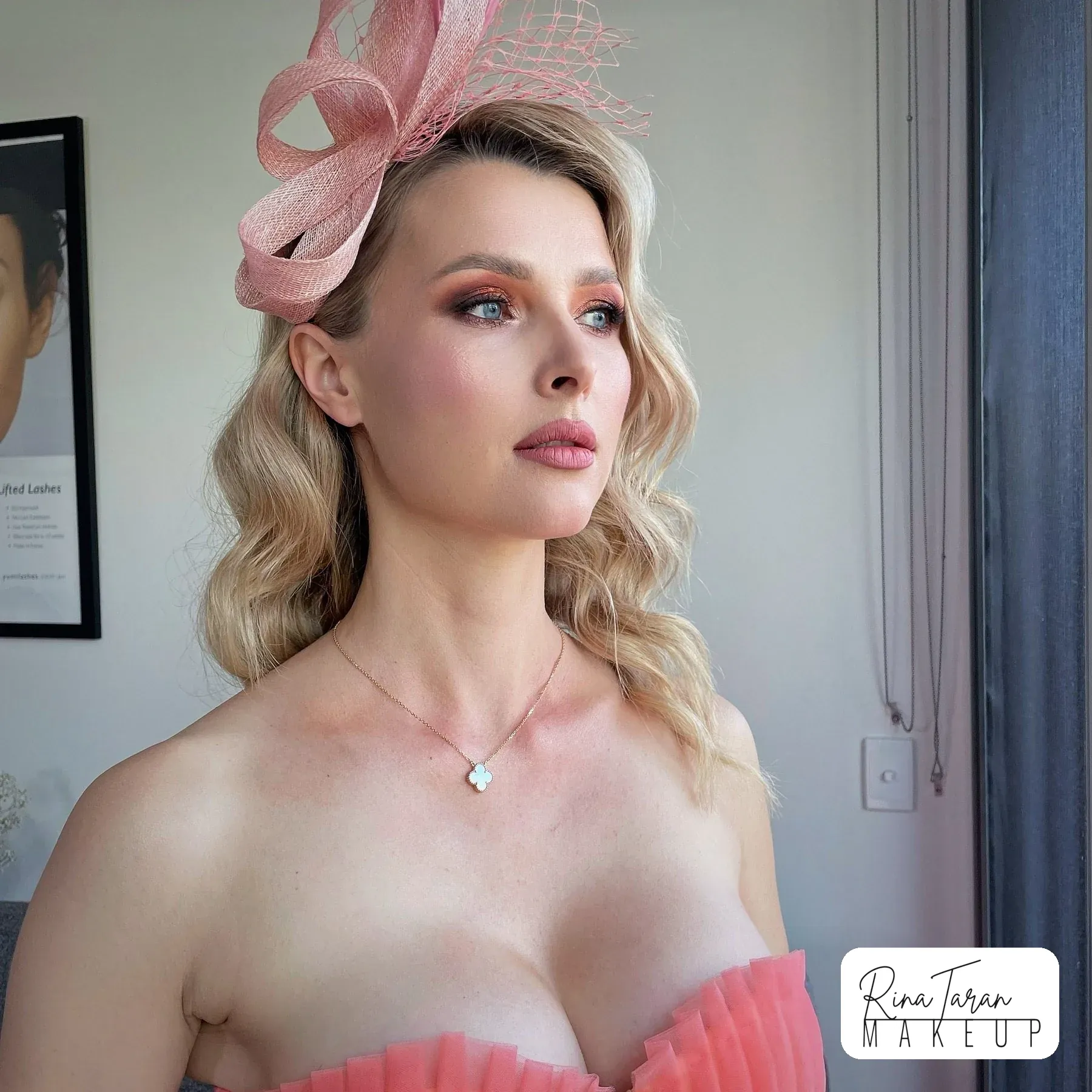 Race day hair styling, hair pinned back with soft tendrils under a pink fascinator, with hair and makeup done in one sitting