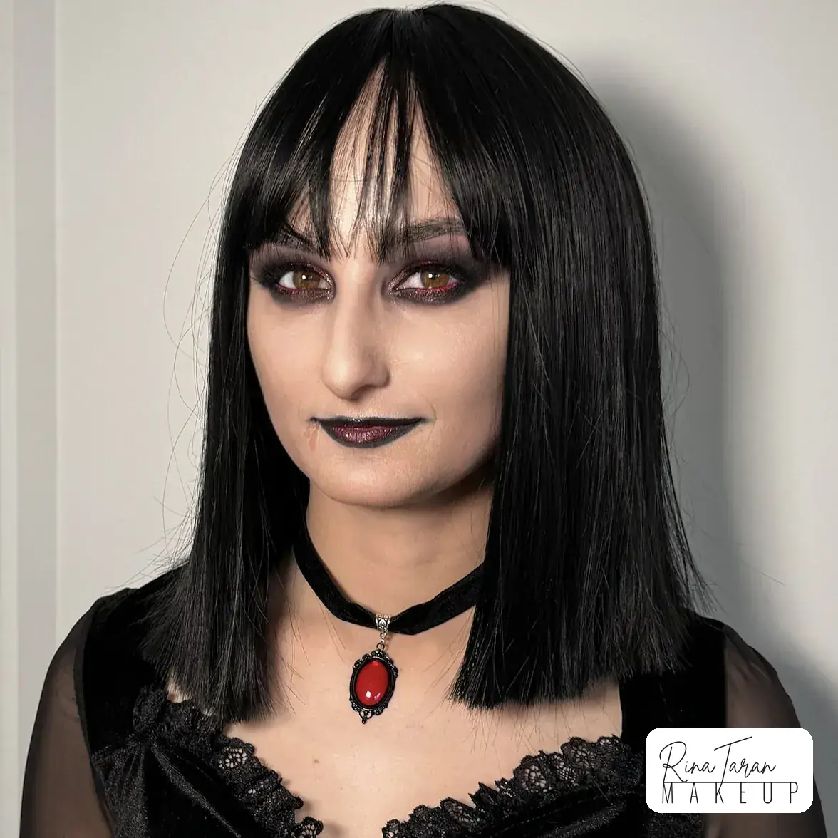 Vampire makeup look with a pale matte face, a black lip and a black bob