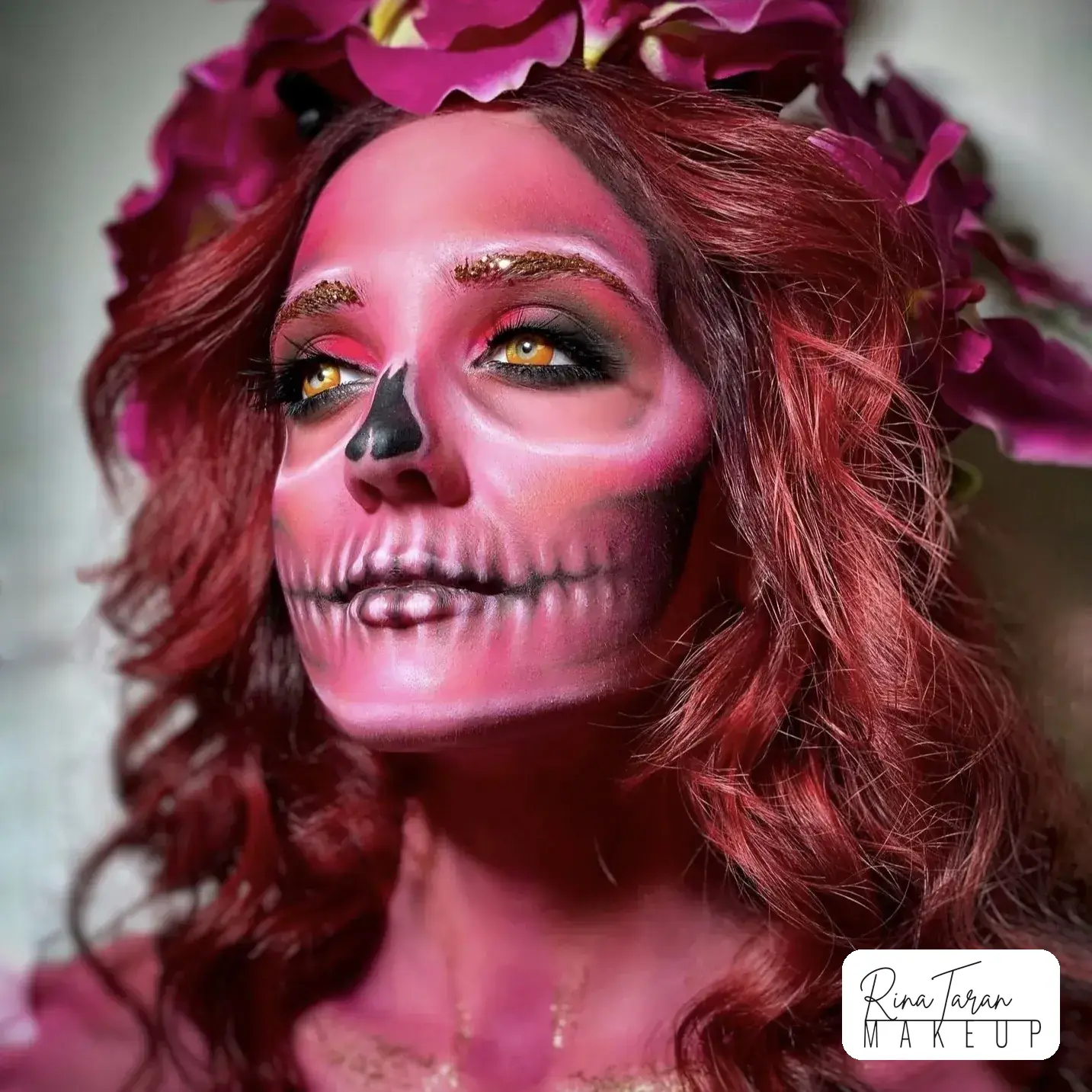 Halloween skull makeup painted over the whole face in pink, with coloured lenses and long red hair