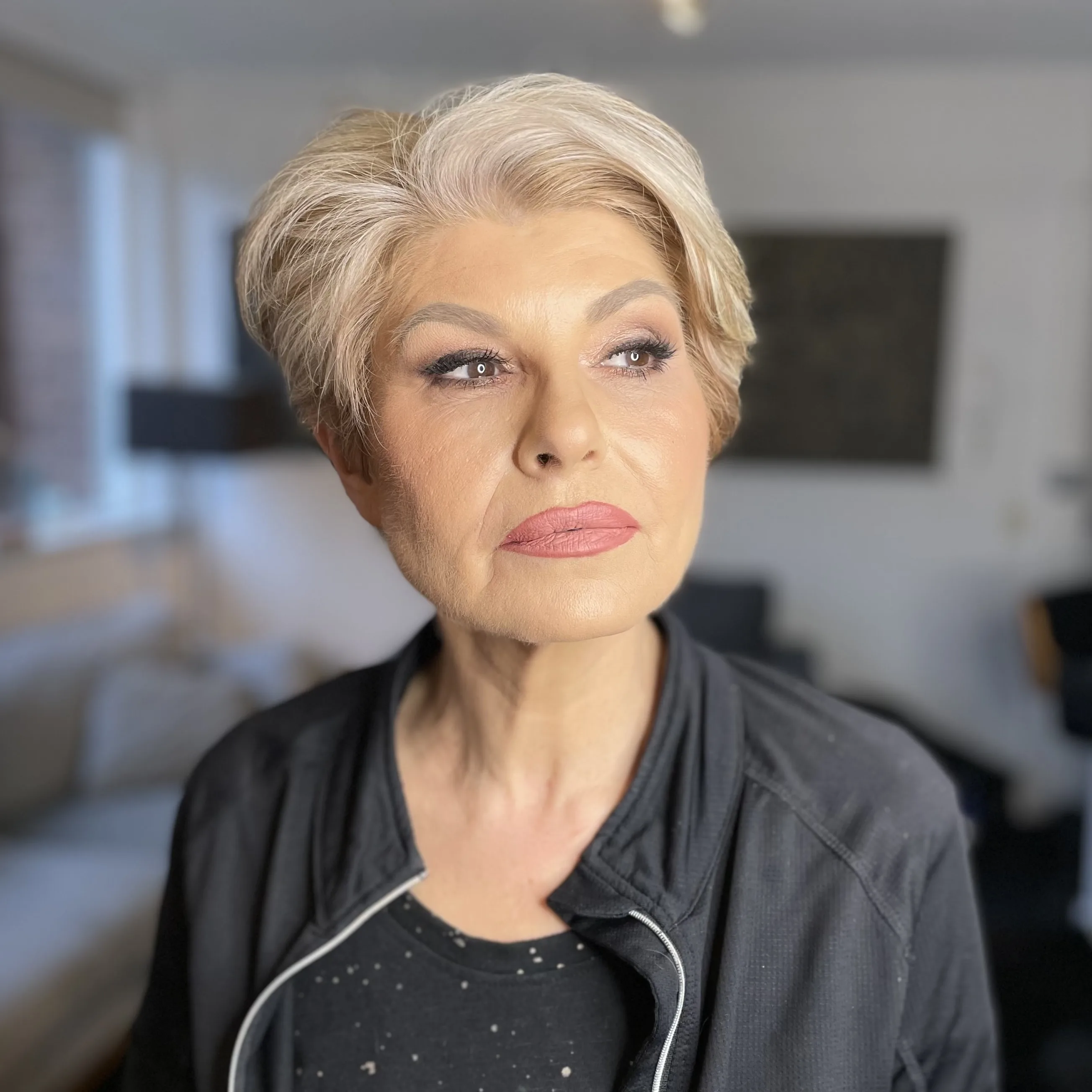 Muted pink lip and a lifted eye on platinum blonde hair, turned to the light