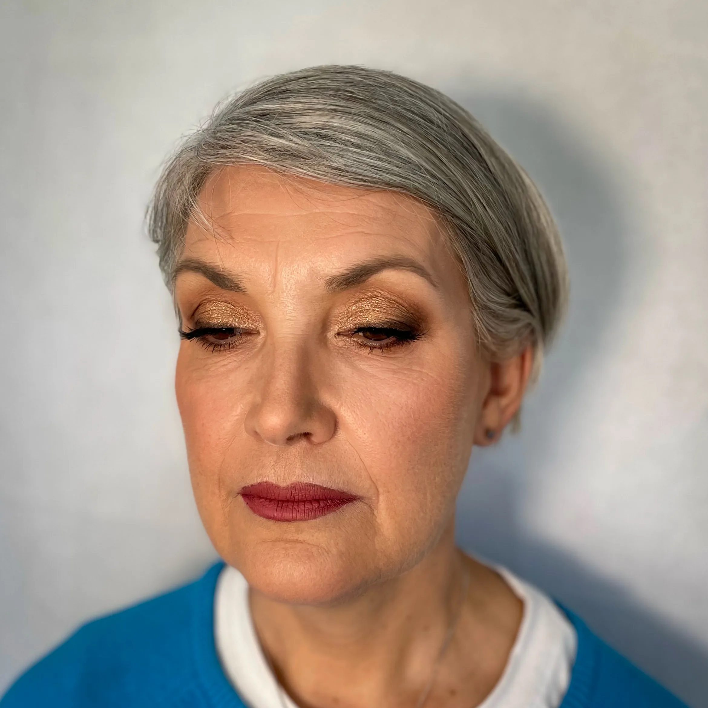 Makeup on mature skin: warm gold shimmer lid and a deep berry lip on silver hair