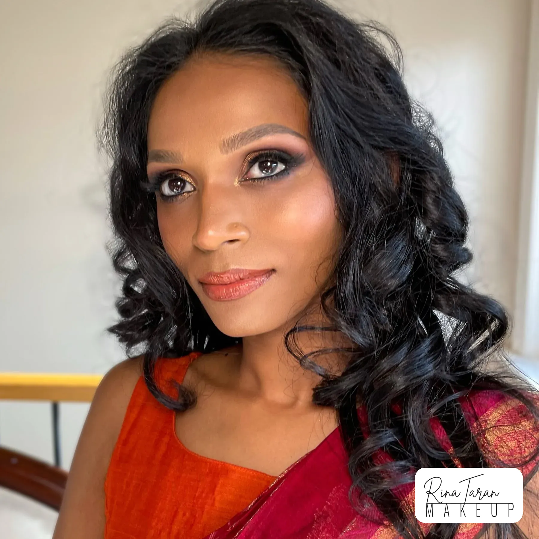 Warm-toned makeup on deep skin, client in an orange and red sari